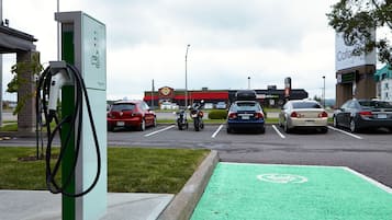 Un estacionamiento con estaciones de carga para vehículos eléctricos, un carril bici verde y un hotel al fondo.