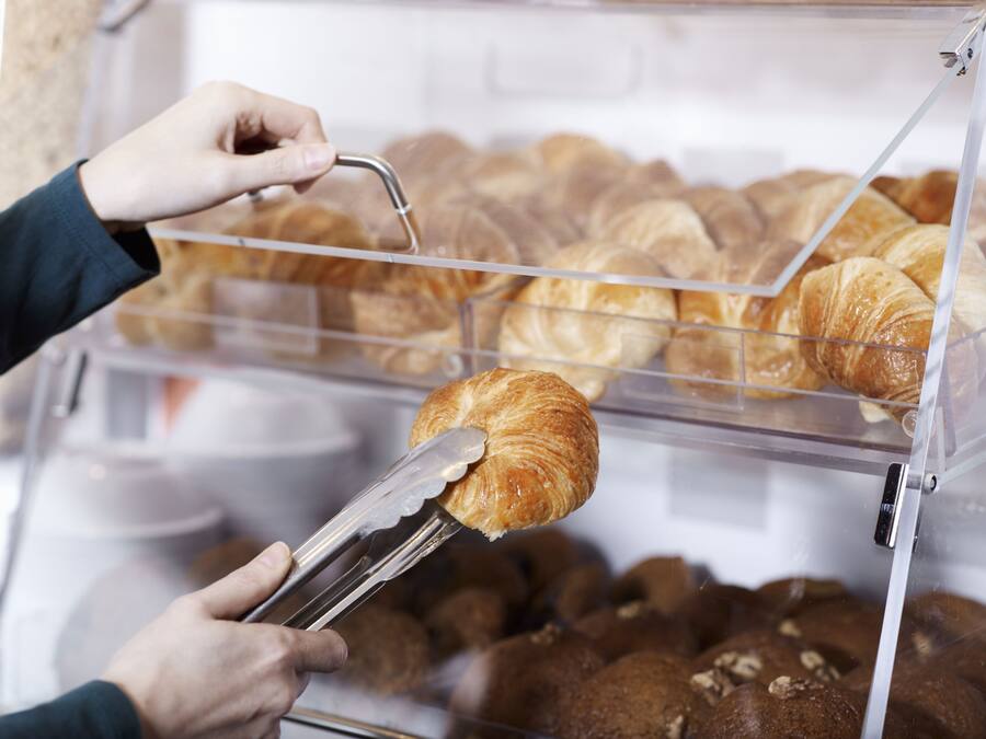 En hånd vælger en croissant fra en bageridisplay.