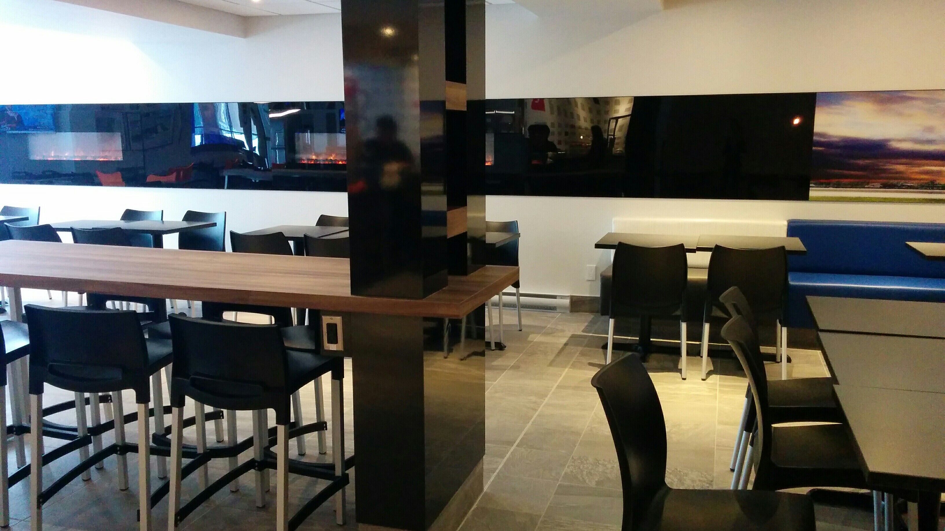 A modern restaurant with a bar area, multiple seating options including bar stools and tables, and a large flat-screen TV mounted on the wall.