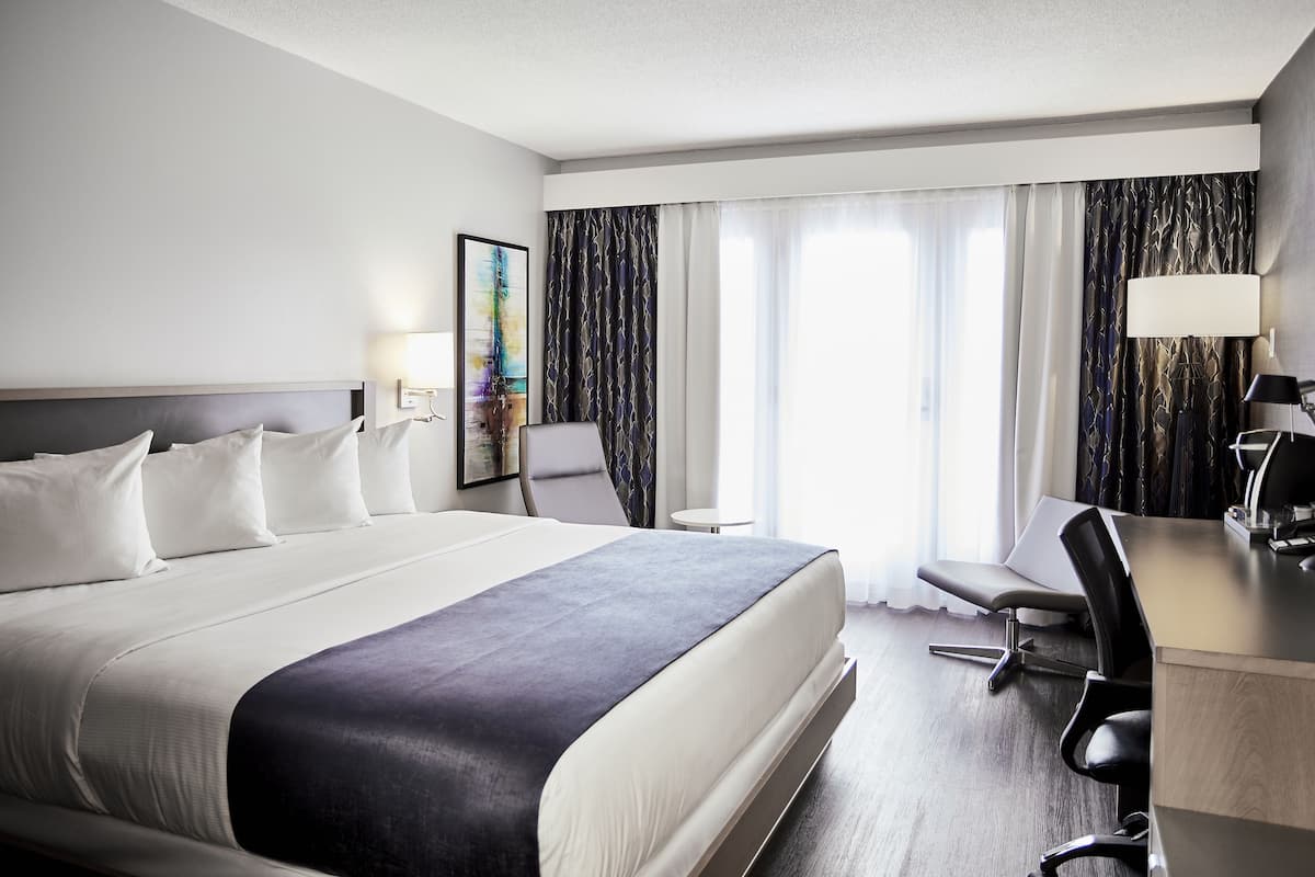 A hotel room with a large bed, a desk, a chair, and a small table.