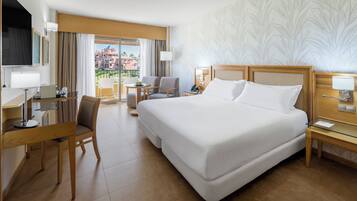 Habitación de hotel con una cama grande, un escritorio con silla, una mesita y vistas a edificios por la ventana.