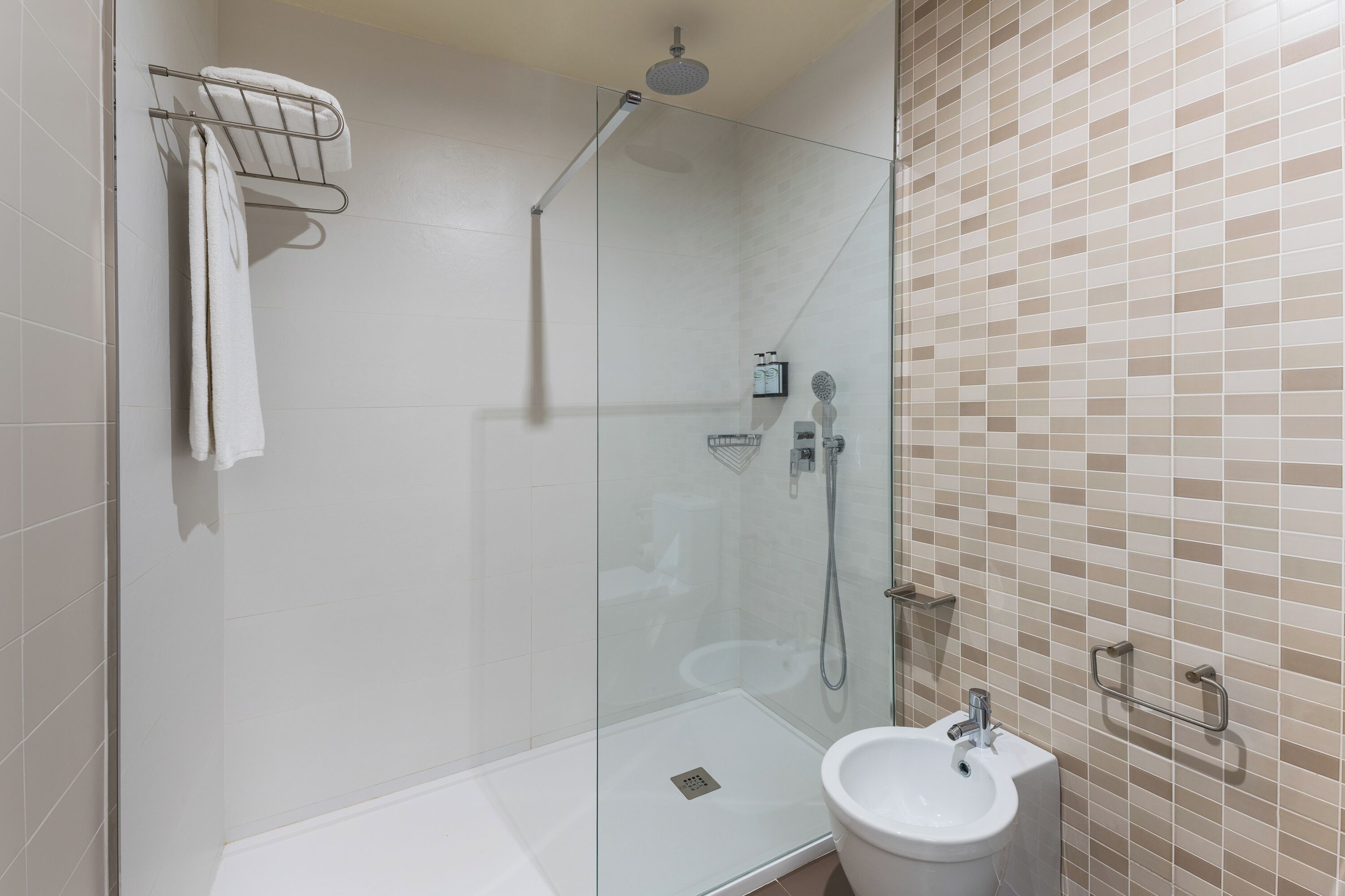 Un baño moderno con ducha de vidrio, un lavabo blanco y pared con azulejos.