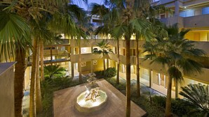 A multi-level hotel courtyard with palm trees, a central fountain, and a well-lit interior. - Elba Costa Ballena Beach & Thalasso Resort (Rota)