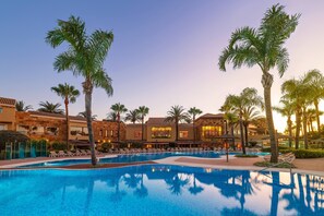 Piscina de resort con palmeras y un edificio con varios balcones.