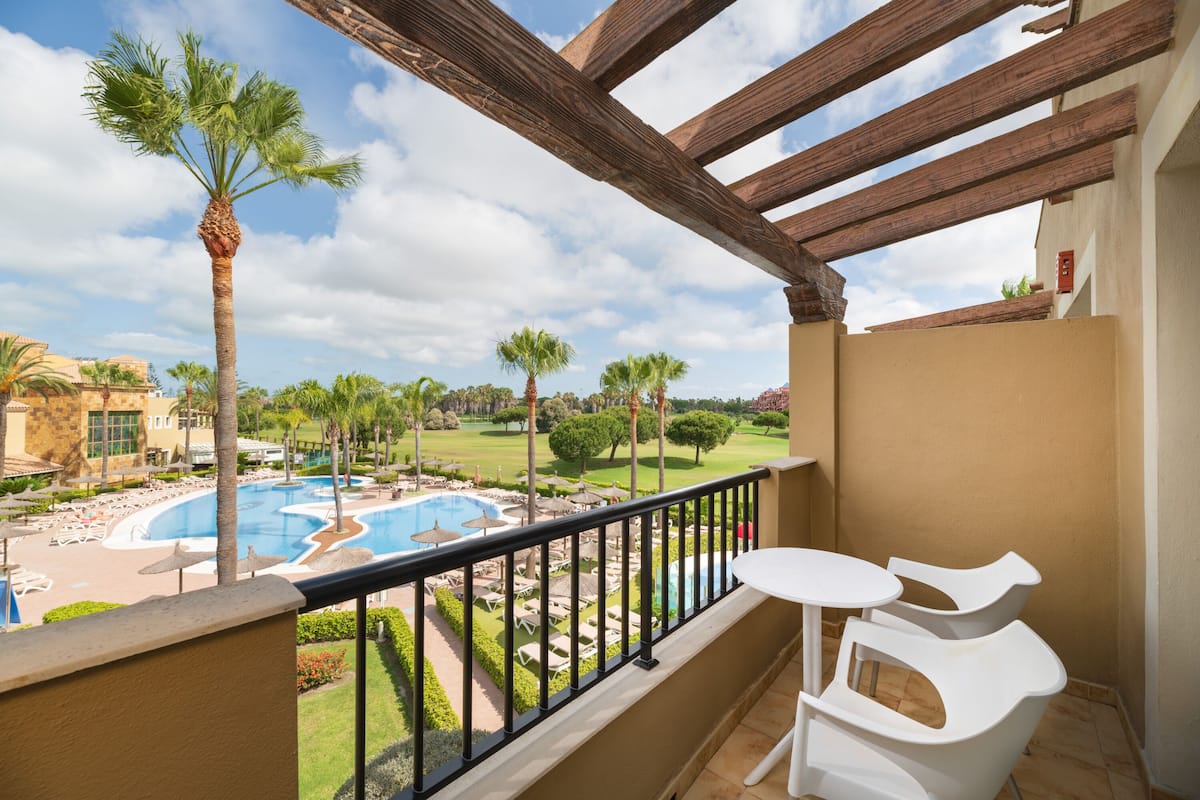 A balcony with a view of a pool, palm trees, and a golf course.