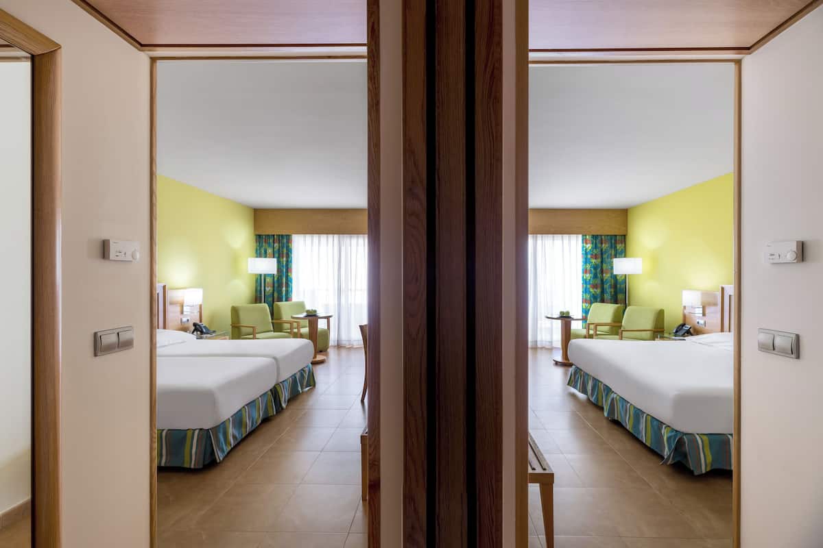 A hotel room with two beds, a desk, chairs, and a window with curtains.