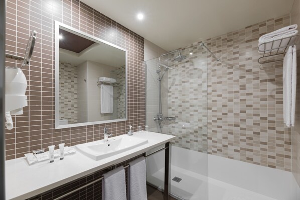 Un baño moderno con un espejo grande, un lavamanos blanco y una zona de ducha con mampara de vidrio.