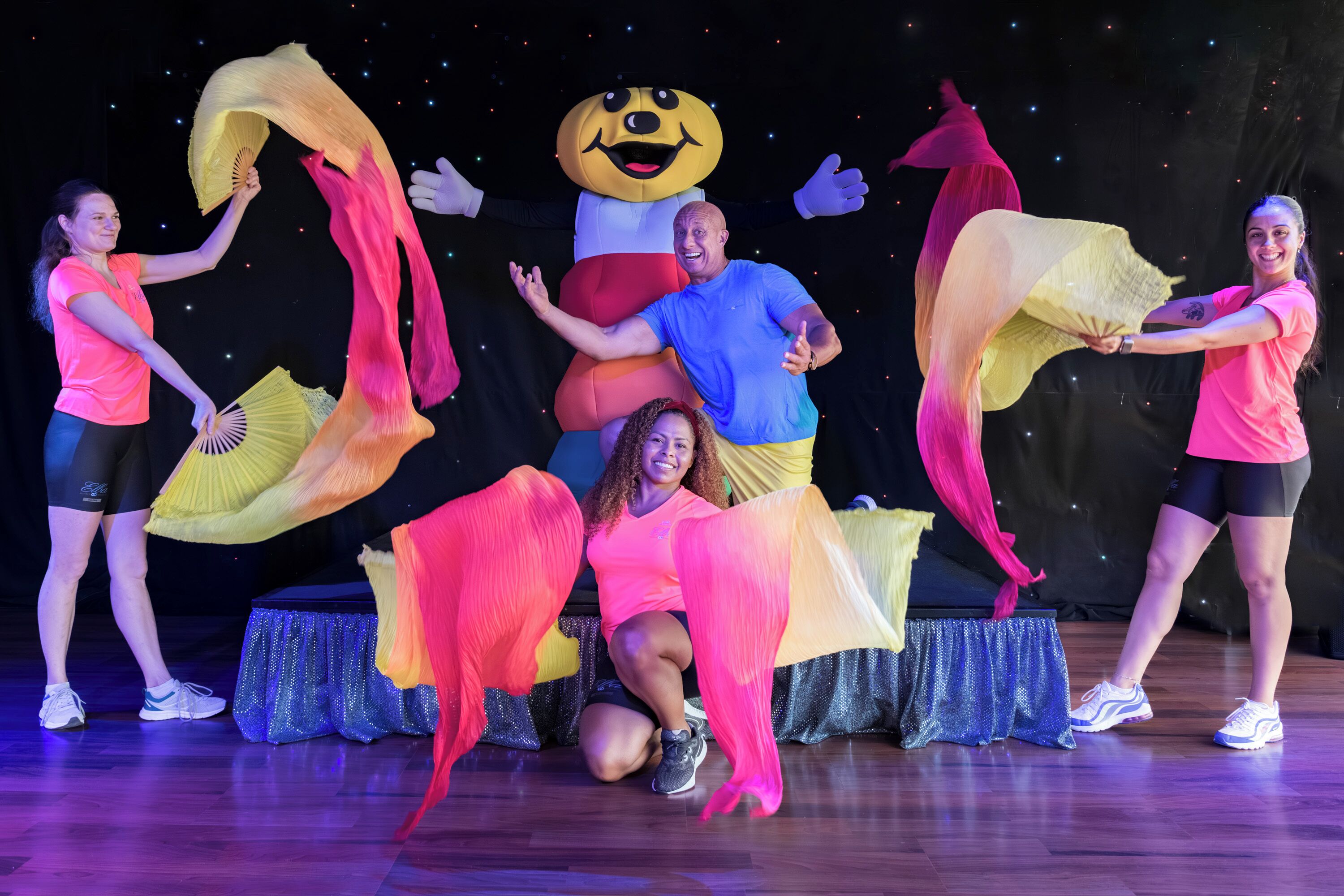 Un escenario con artistas vestidos de rosa y un gran disfraz de mascota.