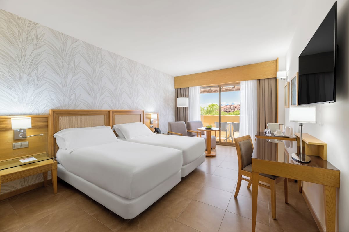 A hotel room with two beds, a desk, a chair, a TV, and a window with a view.