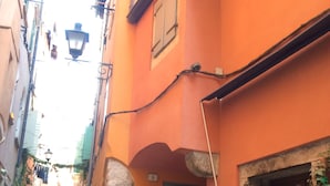 Eine schmale Kopfsteinpflasterstraße, gesäumt von Gebäuden mit steinernen Säulen und einem kleinen Fenster mit Pflanzen.