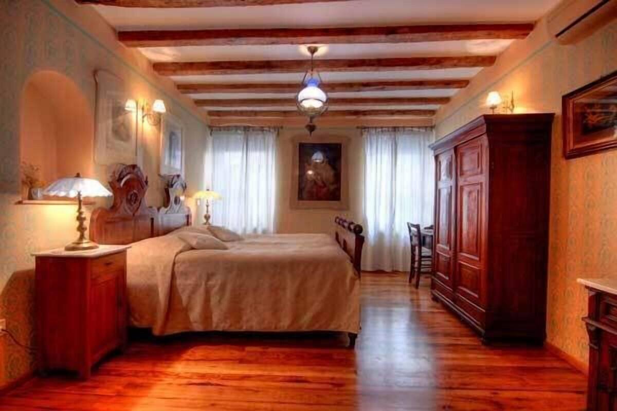 Een slaapkamer met een houten vloer, een bed met een beige deken, een houten garderobe en een schilderij aan de muur.
