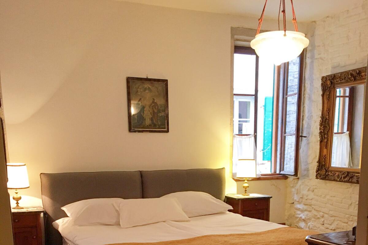 Een slaapkamer met een bed, nachtkastje, lamp, vloerkleed, kledingkast en een schilderij aan de muur.