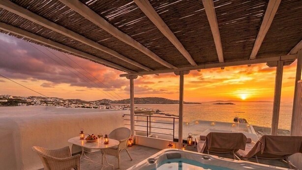 A rooftop terrace with a hot tub, lounge chairs, and a table with candles, overlooking a sunset over the sea. - Mykonos View (Mykonos)