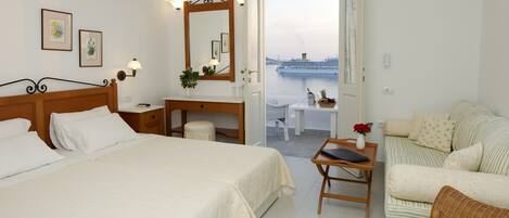 A hotel room with a bed, a desk, a chair, a small table with a vase, and a view of a cruise ship.