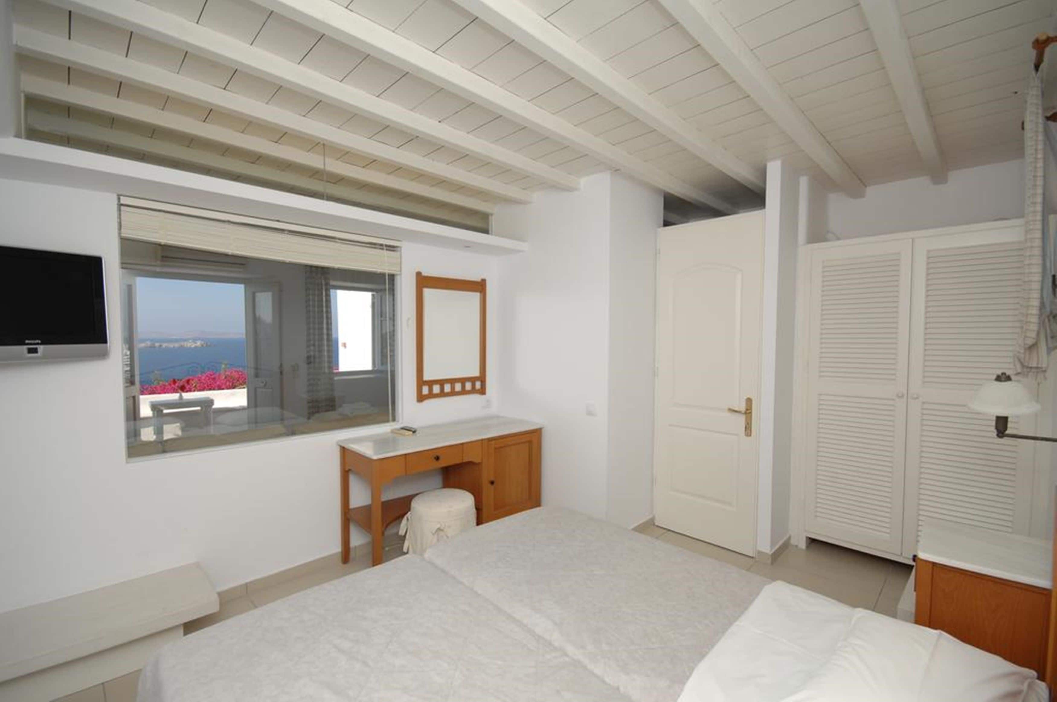 Een slaapkamer met een bed, een bureau, een spiegel, een televisie en een raam met uitzicht.