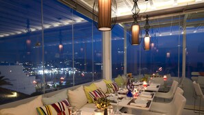 A restaurant with tables set for dining, large windows offering a city view, and hanging pendant lights. - Mykonos View (Mykonos)