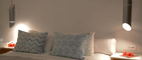 Una cama bien tendida con almohadas estampadas, una mesita de noche con lámpara y un enchufe en la pared.