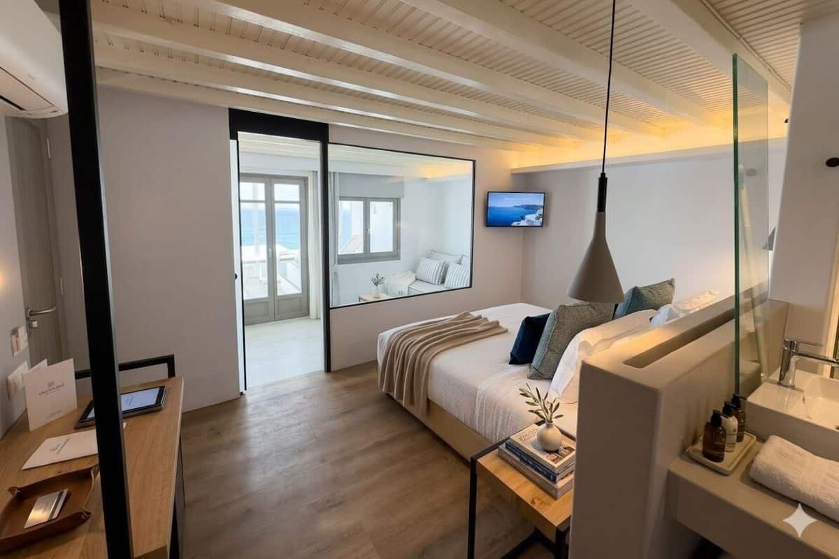 Una habitación de hotel moderna con cama, mesita de noche, televisor y un ventanal grande.