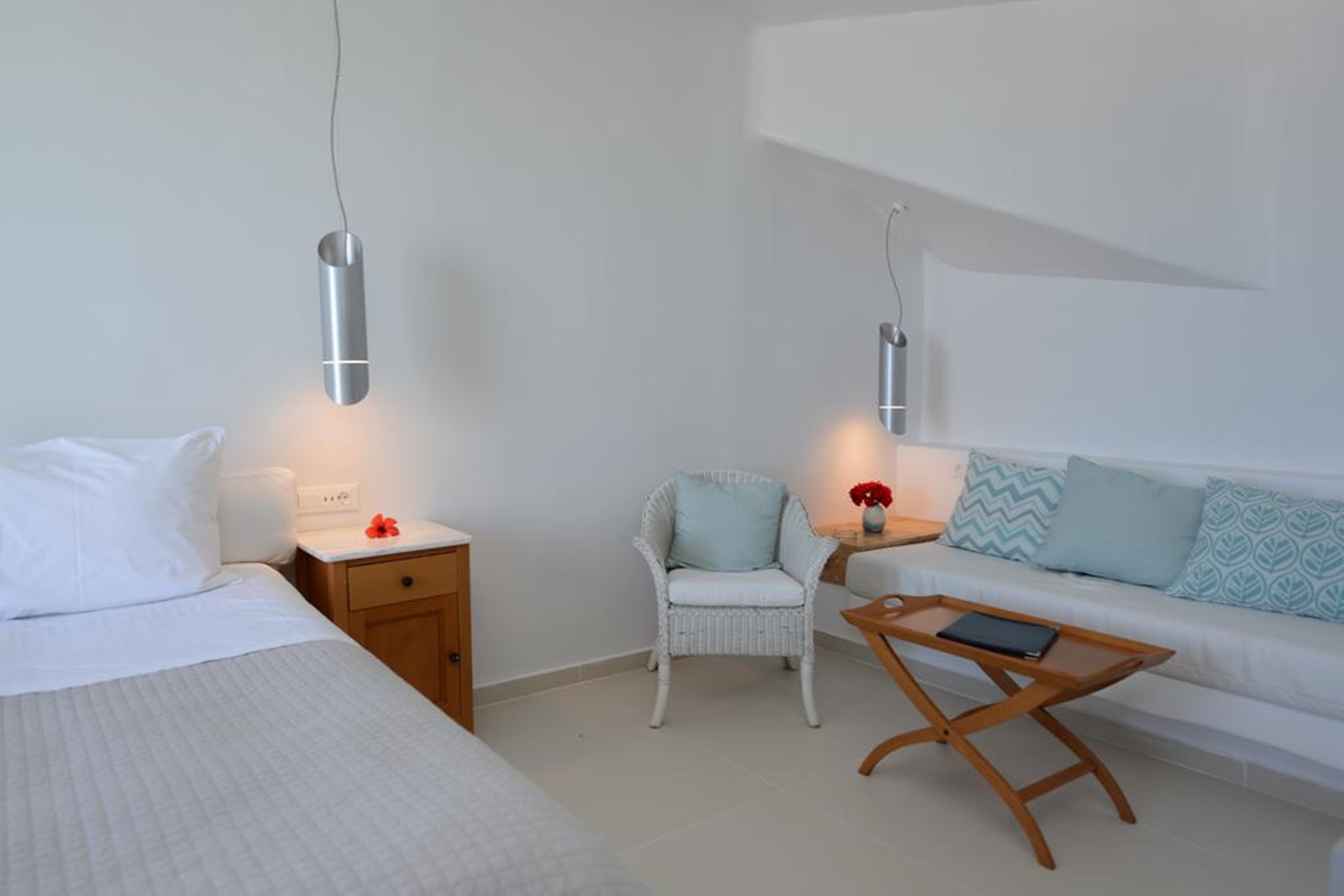 Et minimalistisk hotelværelse med seng, hvid sofa, lille træbord og to sengeborde med vægmonterede lamper.