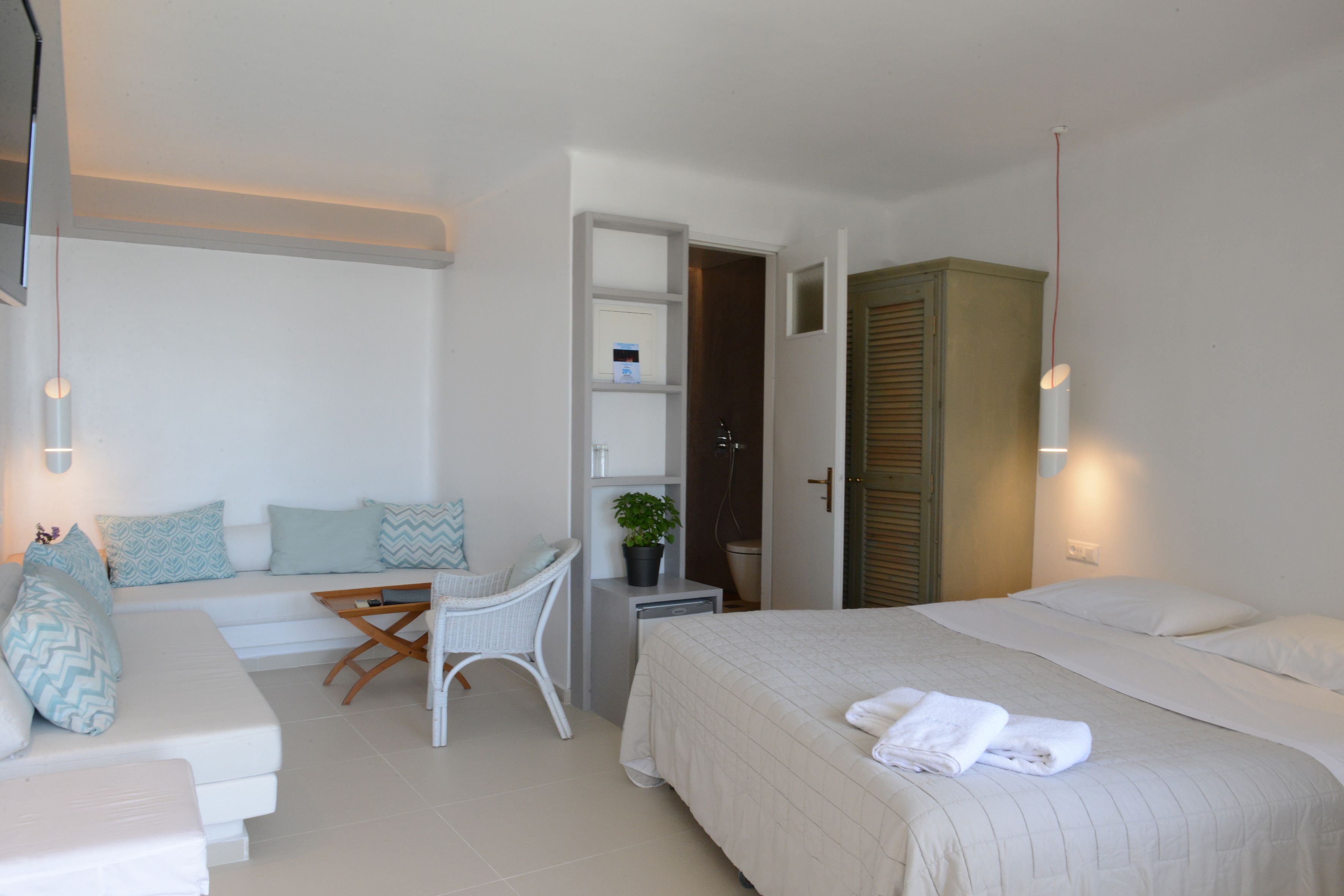 A hotel room with a bed, a sofa, a small table, a chair, a desk, and a bathroom.
