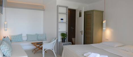 A hotel room with a bed, a sofa, a small table, a chair, a desk, and a bathroom.