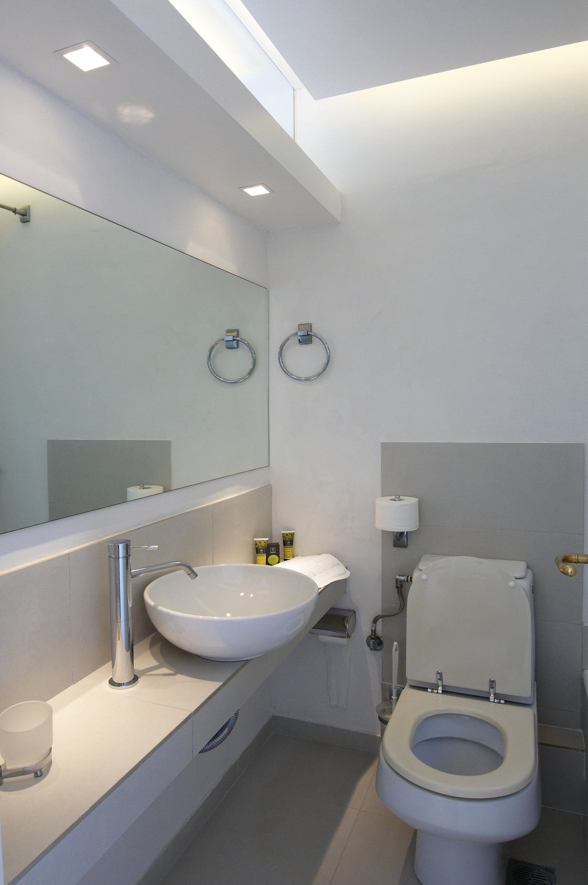 Un baño moderno con un lavamanos, espejo y retrete blancos.