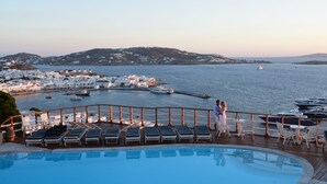 A poolside area with lounge chairs, a view of the sea, and boats. - Mykonos View (Mykonos)