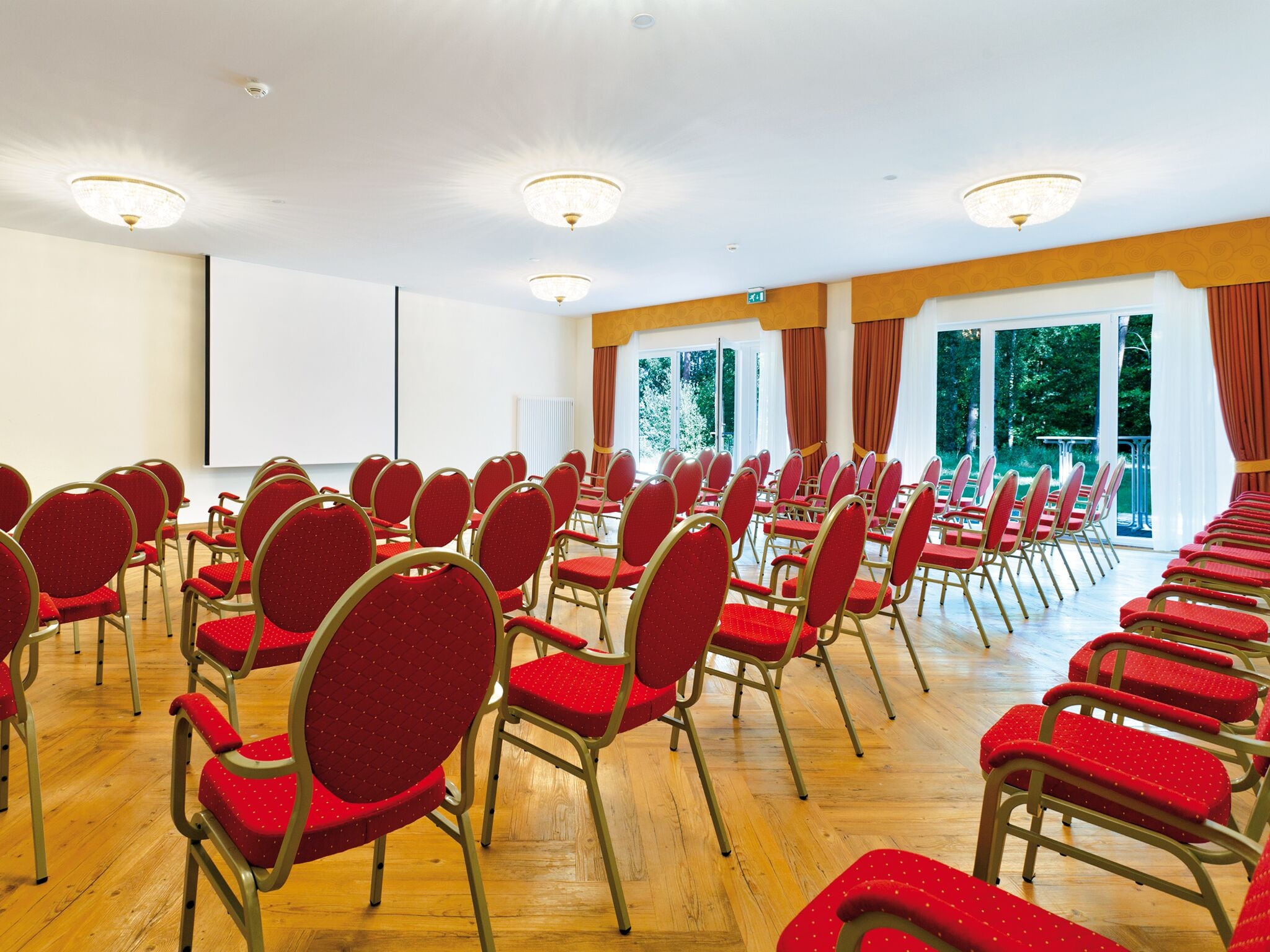 A conference room with rows of red chairs and a large screen at the front.