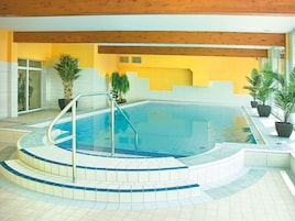 Una piscina interior con suelo de baldosas, techo de madera y plantas en macetas alrededor del área de la piscina.