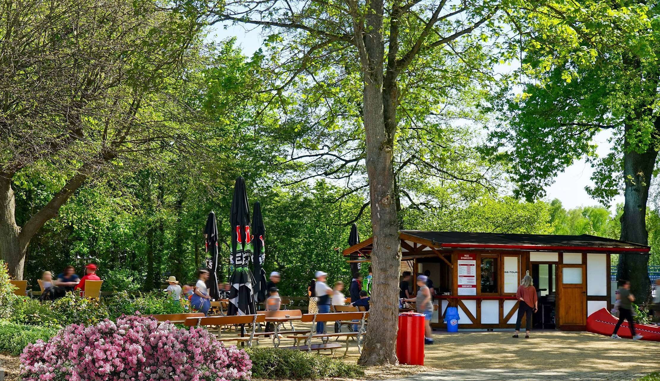 Un parque con mesas de picnic, bancos y una pequeña estructura de madera con un letrero.