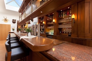 Zona de bar con una barra larga, varios taburetes y una selección de botellas y vasos en estantes.
