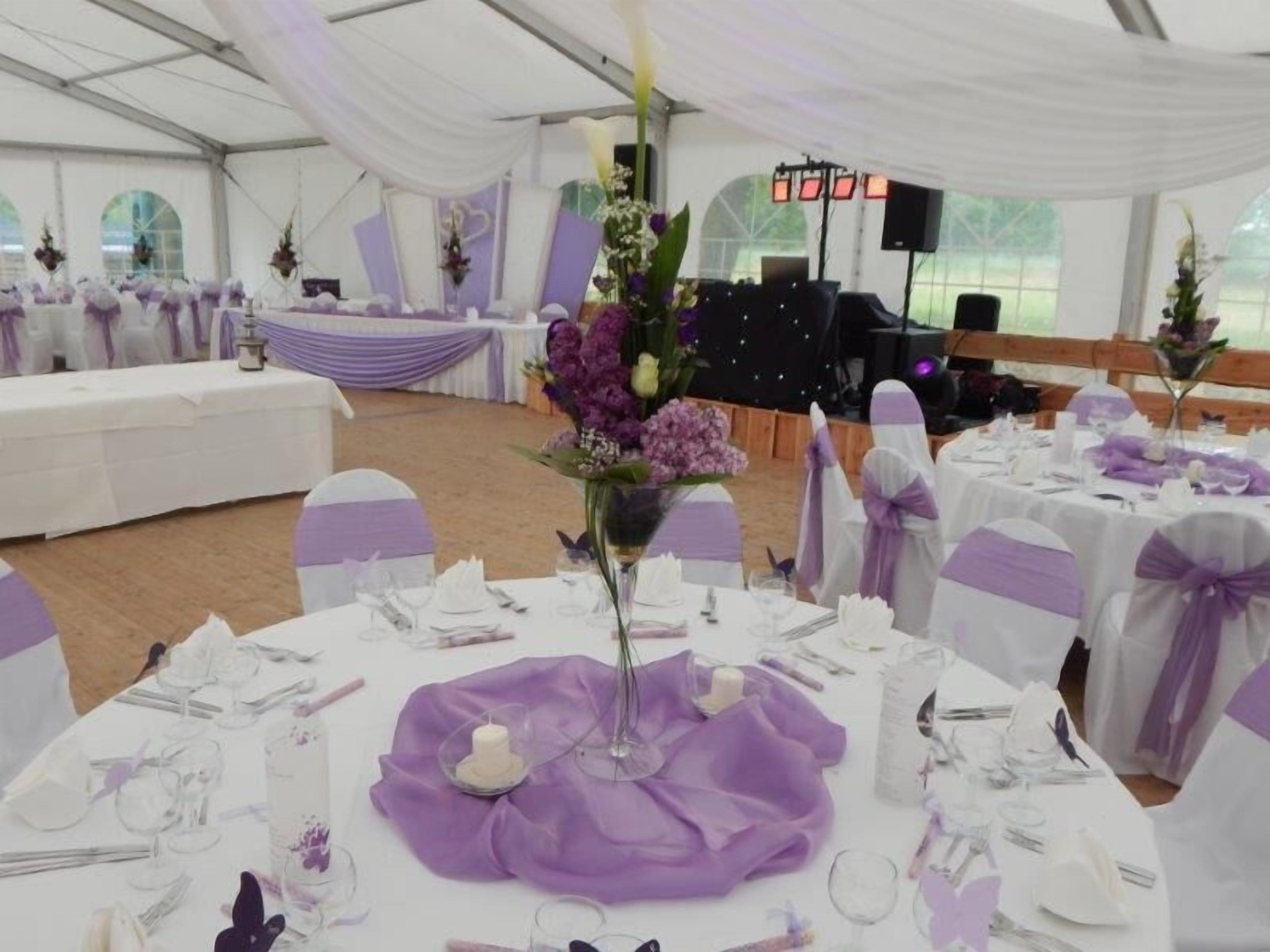 A tented event space with round tables set for dining, featuring purple accents and white tablecloths.
