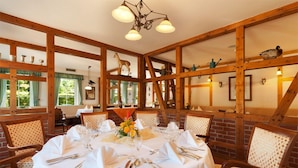 A dining area with a round table set for a meal, wooden beams on the ceiling, and chairs with patterned cushions. - Morada Hotel Isetal (Gifhorn)