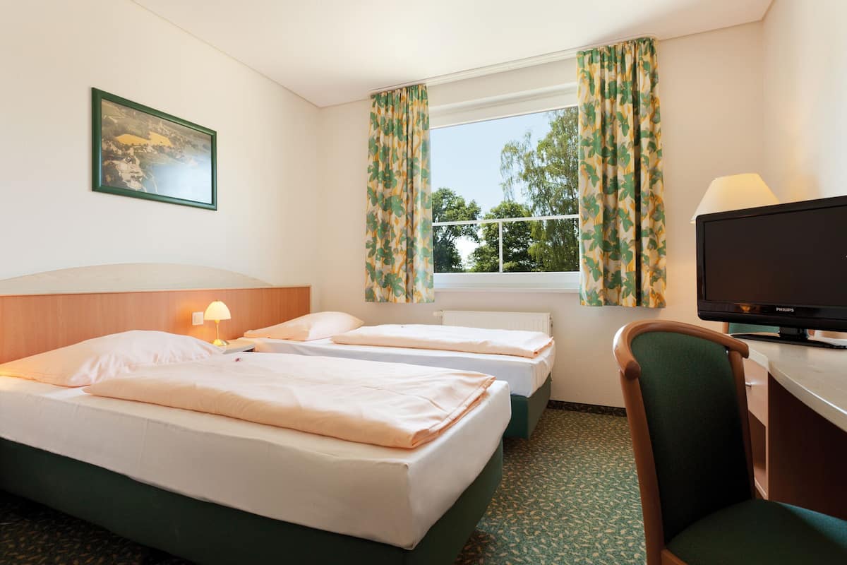 A hotel room with two beds, a desk with a television, and a window with curtains.