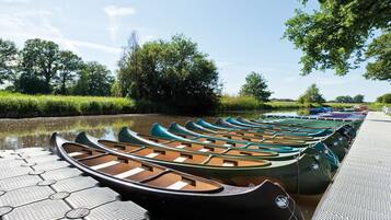 A row of canoes lined up on a dock by a calm river, surrounded by lush greenery.