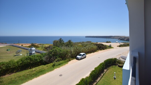 A coastal road with a car, greenery, and a clear view of the sea and cliffs. - Aparthotel Navigator (Vila do Bispo)