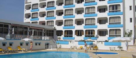 A hotel with a pool area, multiple balconies, and a clear blue sky.