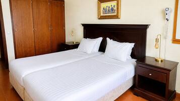 A hotel room with a large bed, wooden wardrobe, bedside tables with lamps, a framed picture on the wall, and a telephone on the wall.