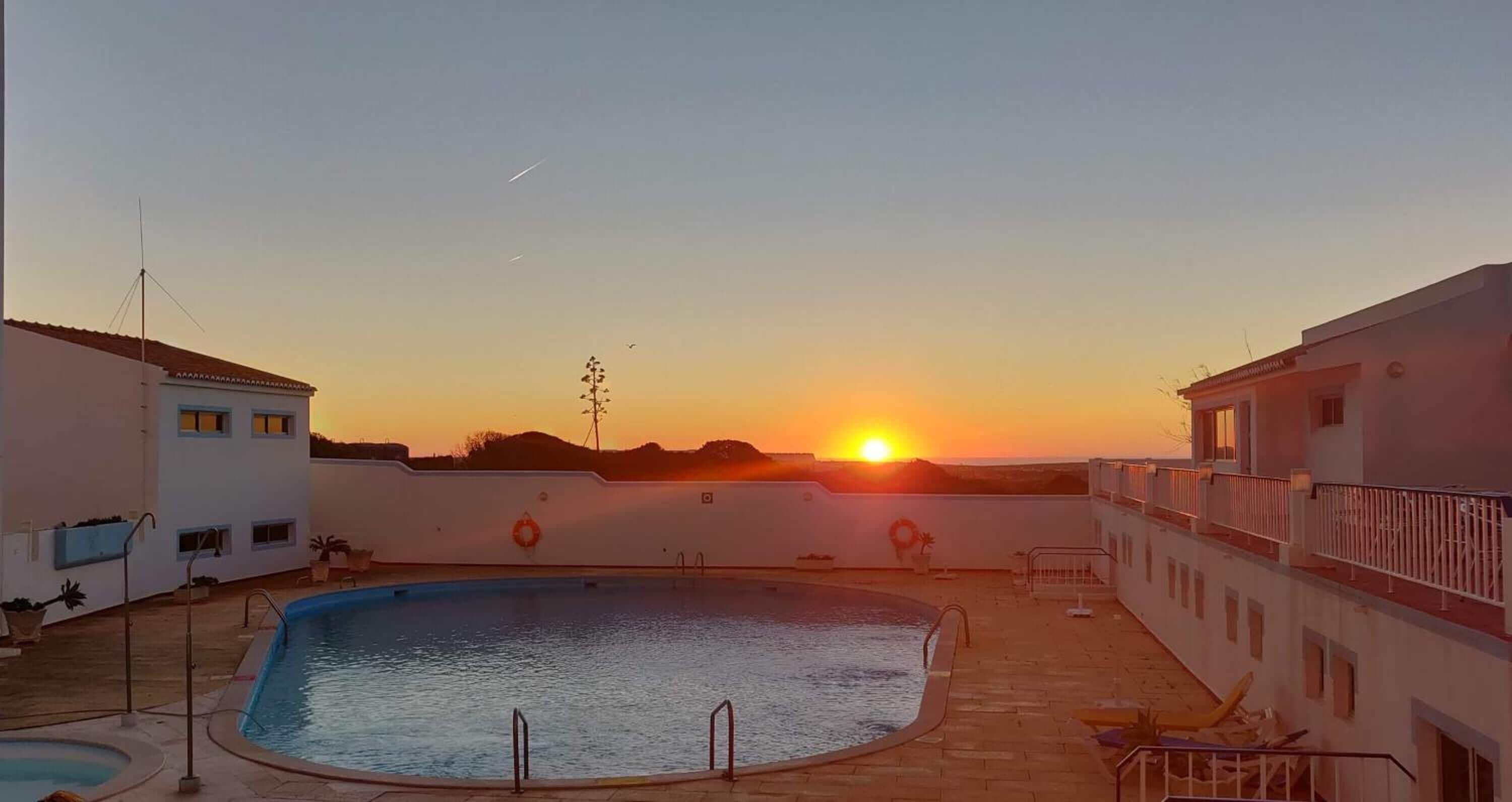 Una piscina con vista al atardecer, rodeada de edificios con balcones y un flotador en la pared.