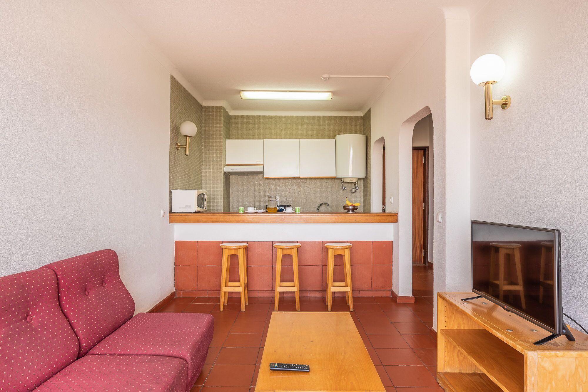 Een compacte woonruimte met een kitchenette, een bank, een televisie en een kleine salontafel.