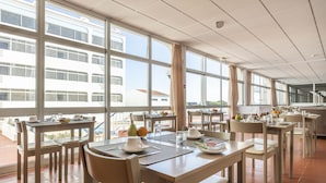 A dining area with multiple tables and chairs, large windows, and a view of buildings outside. - Aparthotel Navigator (Vila do Bispo)