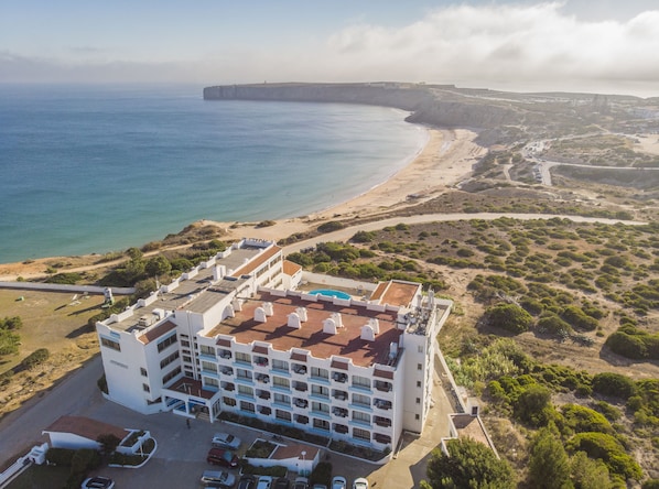 Un hotel frente al mar con varios pisos, piscina y vistas a la playa.