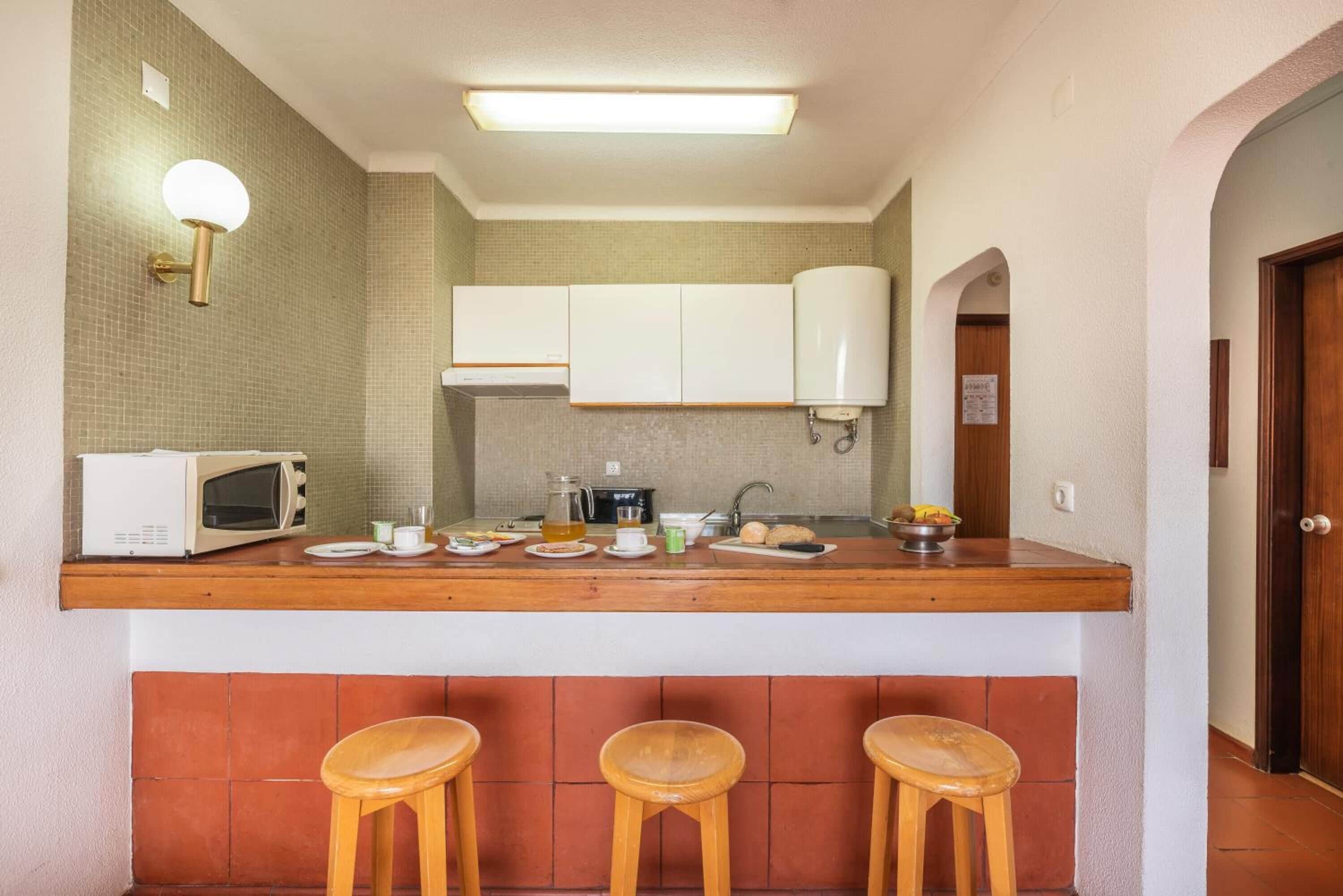 A compact kitchen with a wooden countertop, a microwave, and three stools.
