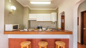 A compact kitchen with a wooden countertop, a microwave, and three stools.