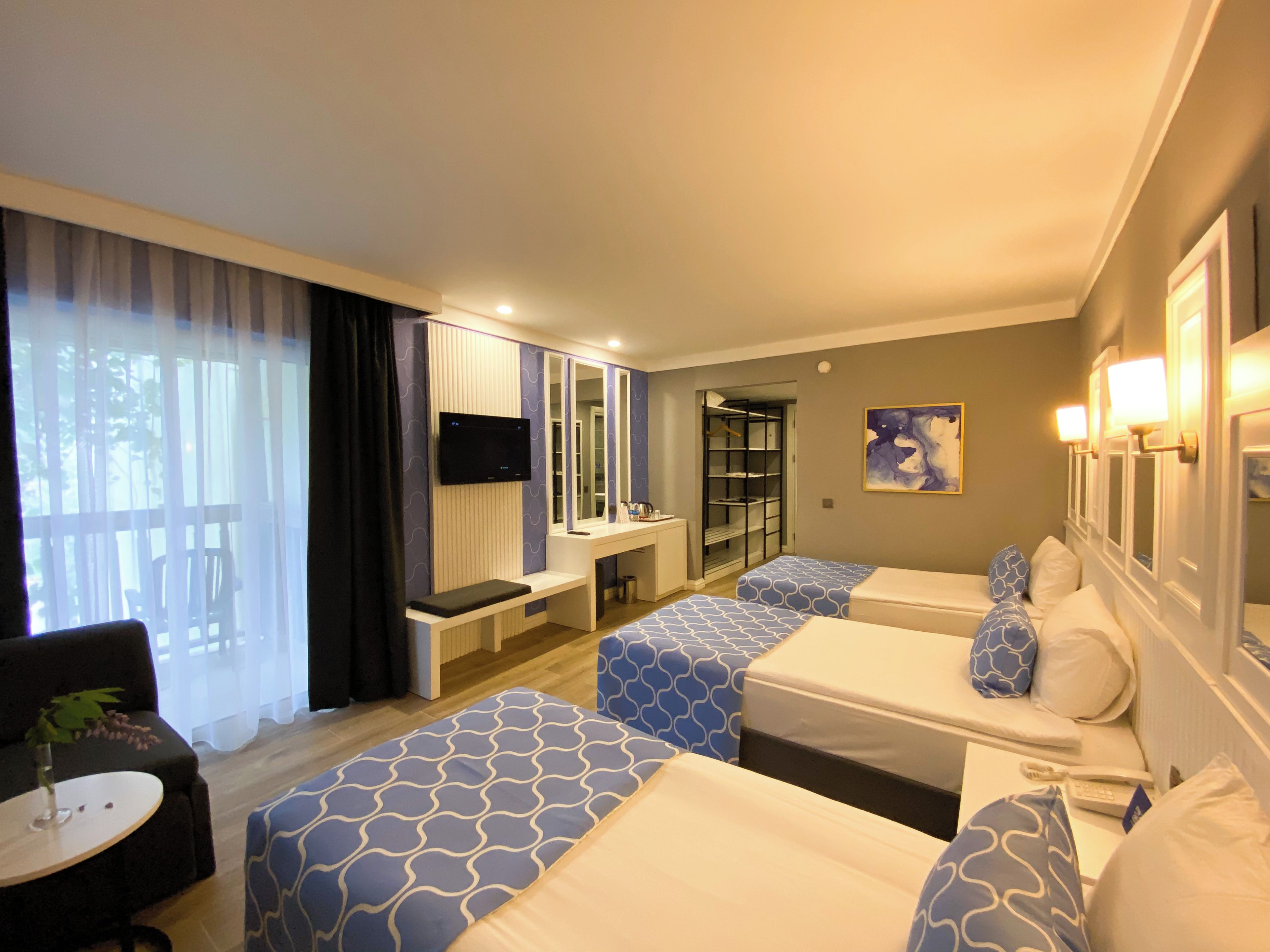 Habitación de hotel con dos camas, un escritorio, una silla, un televisor y una ventana con cortinas.