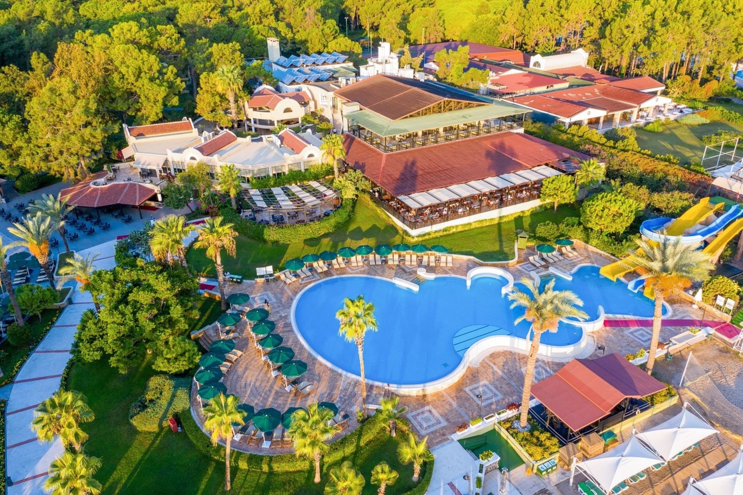 A resort with a large swimming pool, multiple dining areas, and a variety of outdoor seating options.