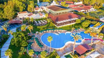 A resort with a large swimming pool, multiple dining areas, and a variety of outdoor seating options.