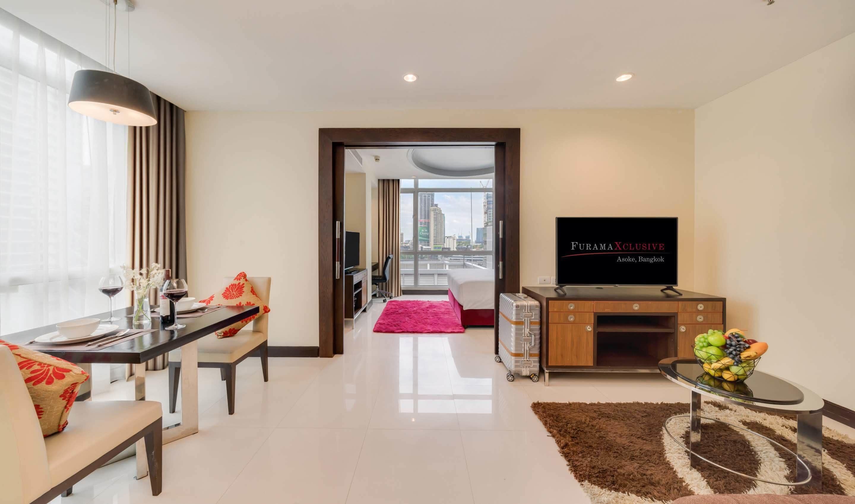 A modern hotel room with a dining area, a TV, and a view of the city.