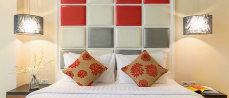 A hotel room with a bed, two decorative pillows, a bedside table with a vase of flowers, and a tray with breakfast items.