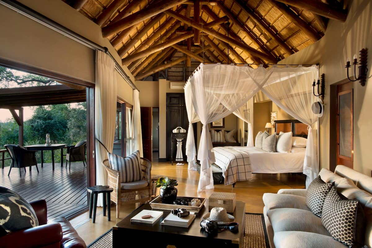 Une chambre spacieuse avec un grand lit, un coin salon avec une table basse et un balcon aménagé avec du mobilier d’extérieur.